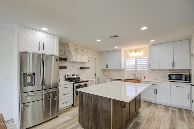 kitchen with sink, stainless steel appliances, white cabinets, a kitchen island, and wall chimney exhaust hood