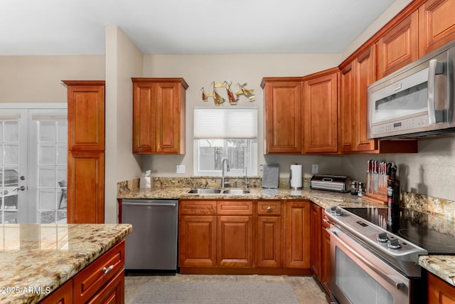 kitchen featuring appliances with stainless steel finishes, brown cabinetry, a sink, and light stone countertops