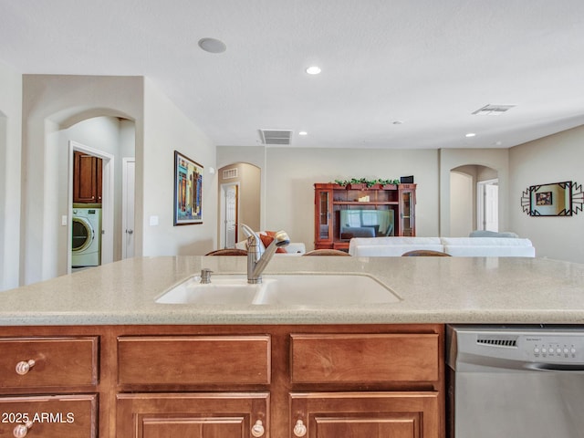 kitchen with a sink, stainless steel dishwasher, arched walkways, and washer / dryer