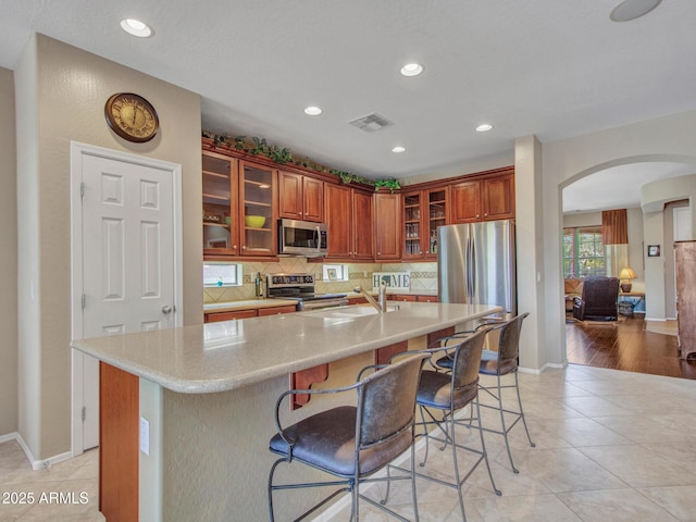 kitchen with stainless steel appliances, visible vents, arched walkways, light countertops, and tasteful backsplash