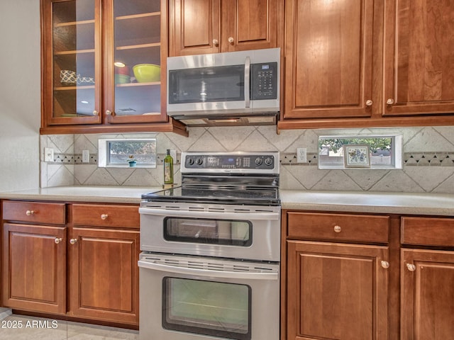 kitchen with light countertops, appliances with stainless steel finishes, decorative backsplash, and glass insert cabinets