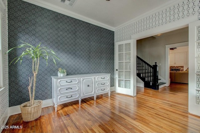 spare room featuring wood finished floors, visible vents, wallpapered walls, stairs, and crown molding