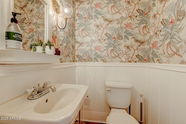 bathroom with toilet, wainscoting, and wallpapered walls