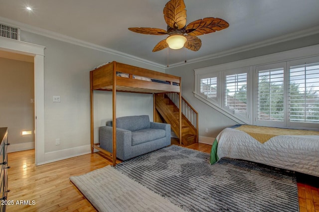 bedroom featuring a ceiling fan, baseboards, wood finished floors, visible vents, and ornamental molding