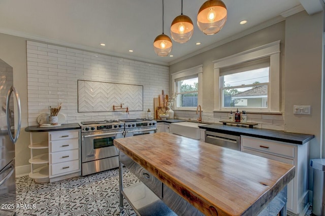 kitchen with a sink, crown molding, appliances with stainless steel finishes, and butcher block counters