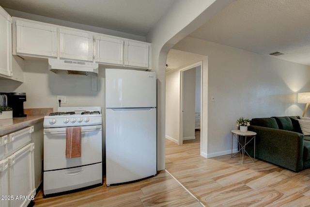 kitchen with under cabinet range hood, white appliances, light wood-style floors, arched walkways, and white cabinets