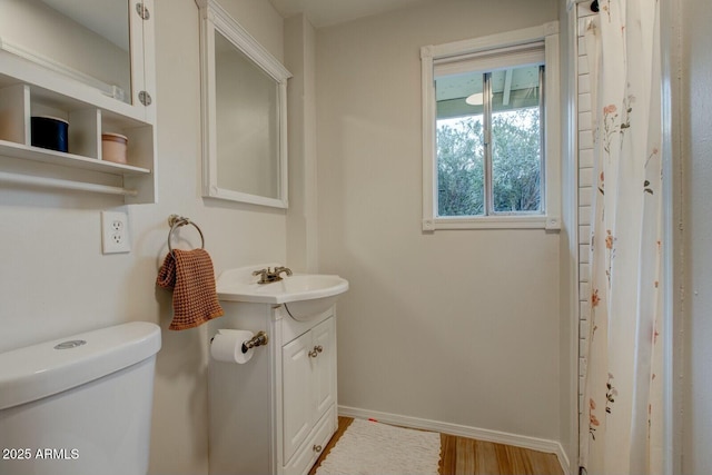 bathroom with toilet, vanity, baseboards, and wood finished floors