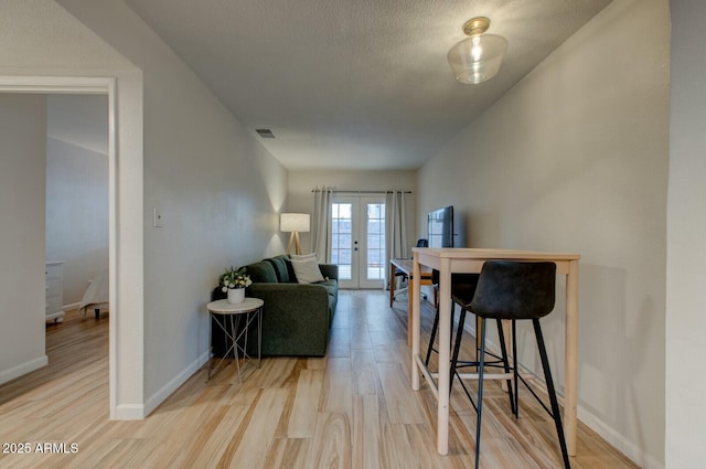 living room featuring visible vents, light wood finished floors, baseboards, french doors, and a textured ceiling