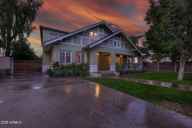 tudor home featuring a gate, stucco siding, a front lawn, and fence