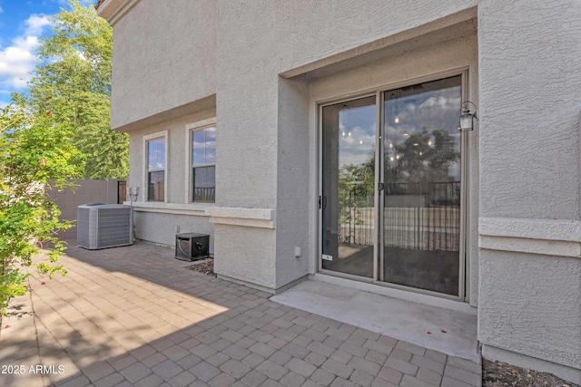 doorway to property with fence, a patio, stucco siding, and central AC unit