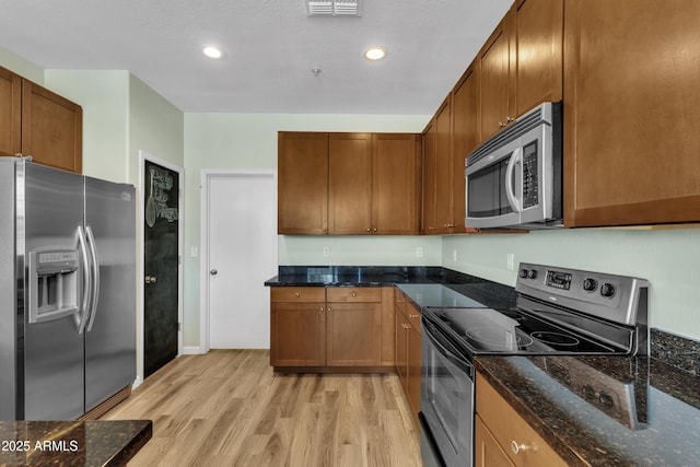 kitchen featuring brown cabinets, light wood-style floors, dark stone counters, stainless steel appliances, and recessed lighting