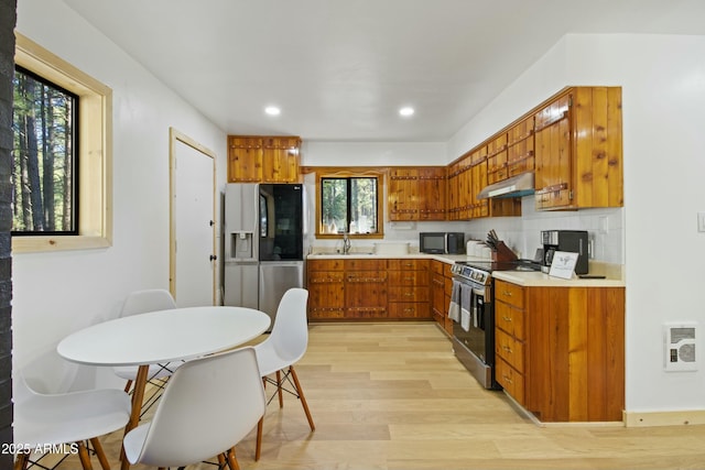 kitchen with a sink, light wood-style floors, brown cabinetry, stainless steel appliances, and under cabinet range hood