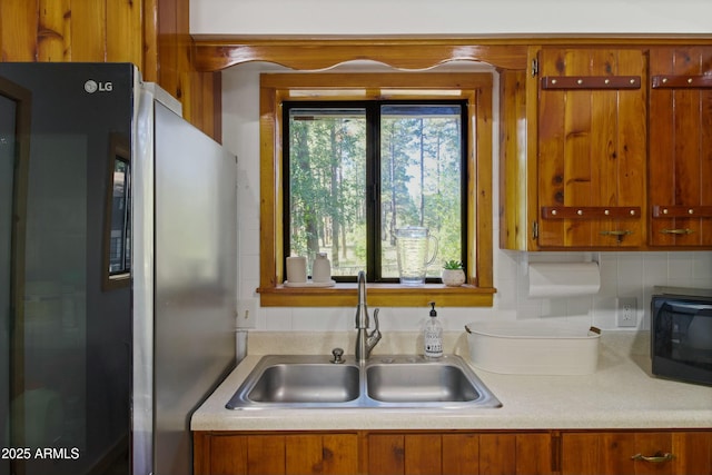kitchen featuring black microwave, brown cabinets, a sink, light countertops, and freestanding refrigerator