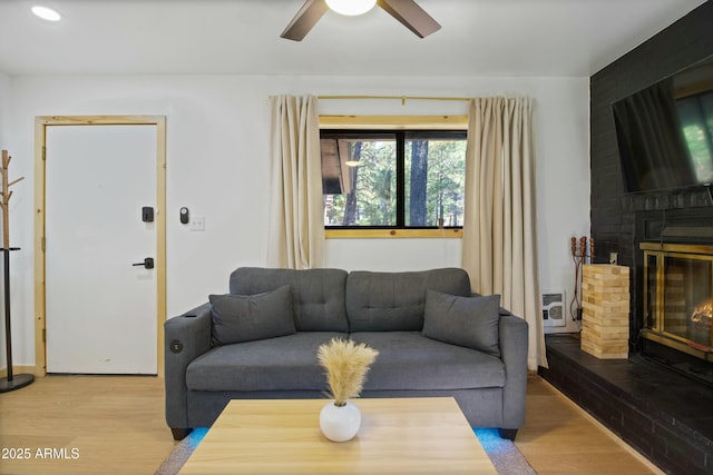 living area with ceiling fan, heating unit, a large fireplace, and wood finished floors