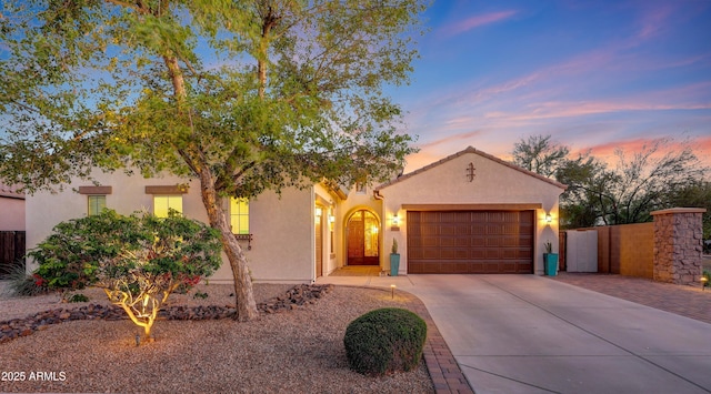 mediterranean / spanish home featuring concrete driveway, fence, stucco siding, and a garage