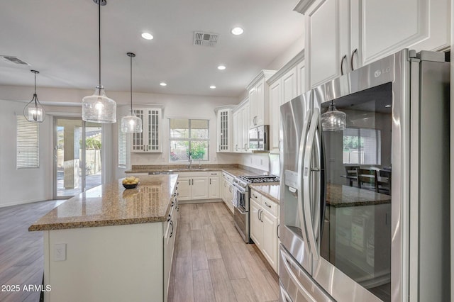 kitchen with appliances with stainless steel finishes, a kitchen island, white cabinetry, and visible vents