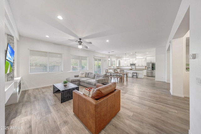 living room with baseboards, ceiling fan, light wood-type flooring, and recessed lighting