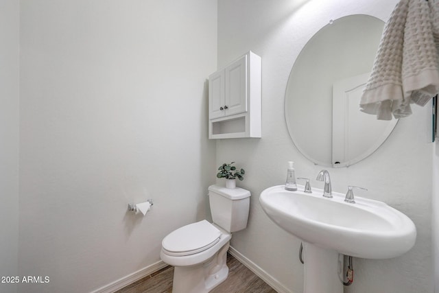 half bathroom featuring toilet, baseboards, a sink, and wood finished floors
