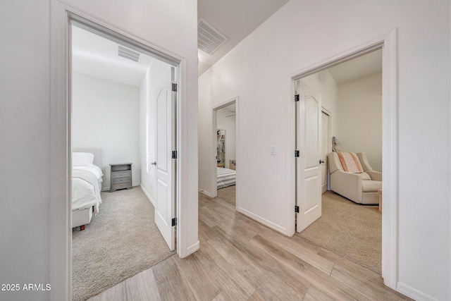 hall featuring baseboards, visible vents, and light wood-type flooring