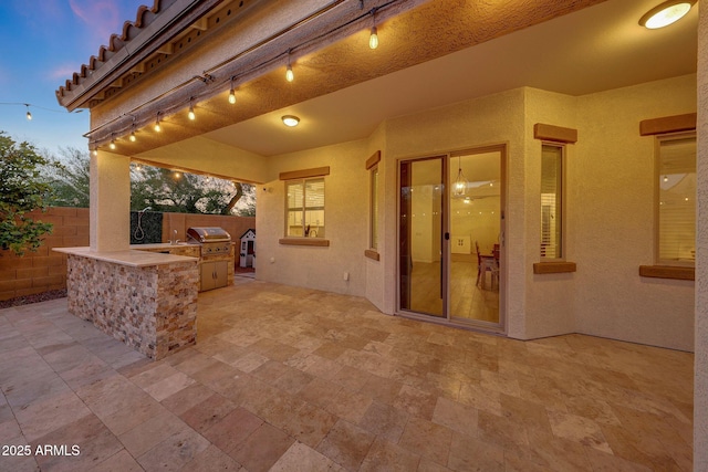 patio terrace at dusk featuring fence, exterior kitchen, and area for grilling