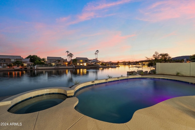 pool at dusk featuring a water view and an in ground hot tub