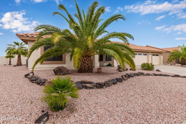 view of front facade featuring concrete driveway, a tiled roof, a garage, and stucco siding