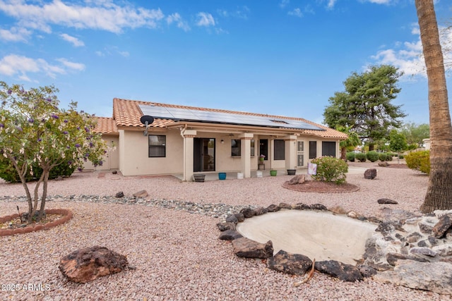 rear view of property featuring a porch, stucco siding, solar panels, and a tiled roof