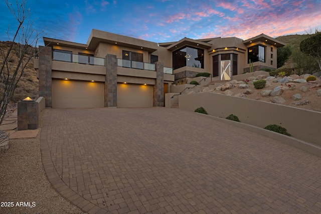 view of front of house with decorative driveway, a balcony, an attached garage, and stucco siding