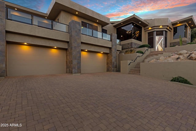 view of front of house featuring stone siding, stairway, an attached garage, decorative driveway, and stucco siding