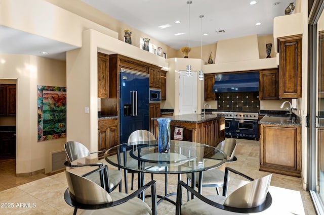 kitchen with built in appliances, light tile patterned floors, a sink, wall chimney exhaust hood, and an island with sink