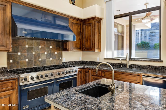 kitchen with appliances with stainless steel finishes, brown cabinetry, a sink, dark stone counters, and extractor fan