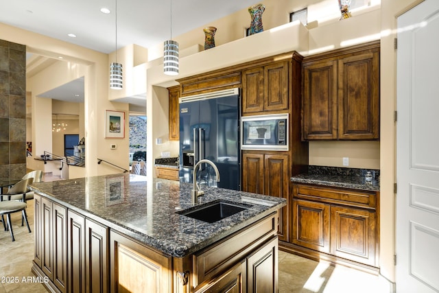 kitchen with high quality fridge, a sink, hanging light fixtures, built in microwave, and dark stone counters