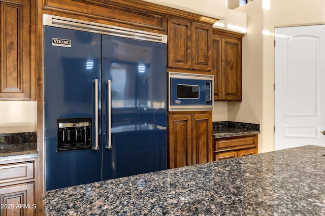 kitchen featuring high end fridge, dark stone countertops, and built in microwave