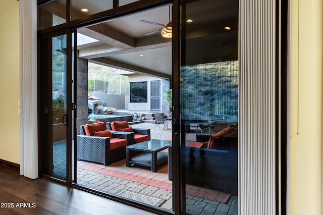 doorway with beam ceiling, a ceiling fan, a wall of windows, and wood finished floors