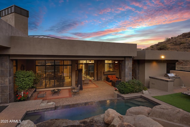 back of property at dusk featuring exterior kitchen and a patio