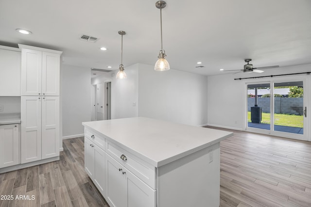 kitchen with decorative light fixtures, white cabinetry, a center island, ceiling fan, and light hardwood / wood-style floors