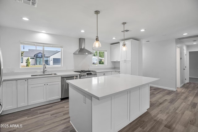 kitchen featuring wall chimney exhaust hood, sink, a center island, stainless steel appliances, and white cabinets