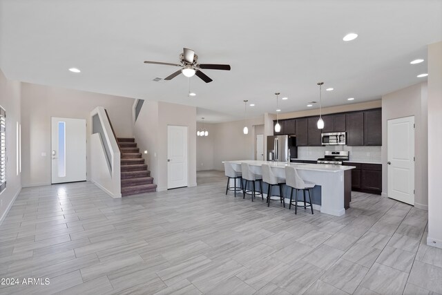 kitchen with dark brown cabinetry, pendant lighting, a center island with sink, ceiling fan with notable chandelier, and appliances with stainless steel finishes