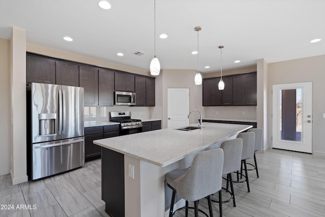 kitchen featuring tasteful backsplash, light stone counters, stainless steel appliances, pendant lighting, and an island with sink