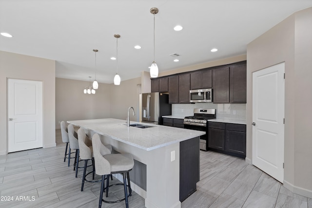 kitchen featuring dark brown cabinetry, sink, stainless steel appliances, decorative light fixtures, and a center island with sink