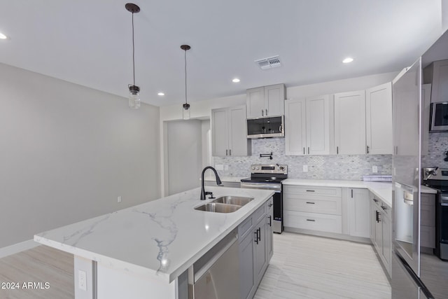 kitchen with tasteful backsplash, appliances with stainless steel finishes, a kitchen island with sink, sink, and decorative light fixtures