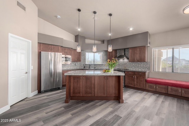 kitchen with stainless steel appliances, visible vents, hanging light fixtures, wall chimney range hood, and light stone countertops