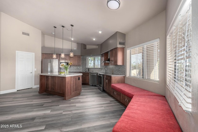 kitchen featuring decorative light fixtures, light countertops, appliances with stainless steel finishes, a kitchen island, and wall chimney range hood