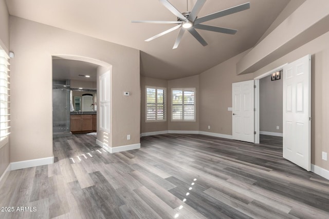 interior space featuring arched walkways, lofted ceiling, a ceiling fan, dark wood-type flooring, and baseboards