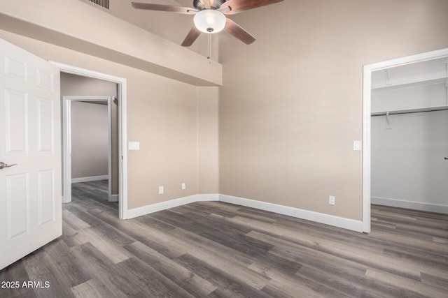 unfurnished bedroom featuring a closet, dark wood finished floors, a walk in closet, and baseboards