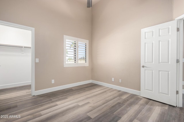 unfurnished bedroom with a closet, a spacious closet, baseboards, and wood finished floors