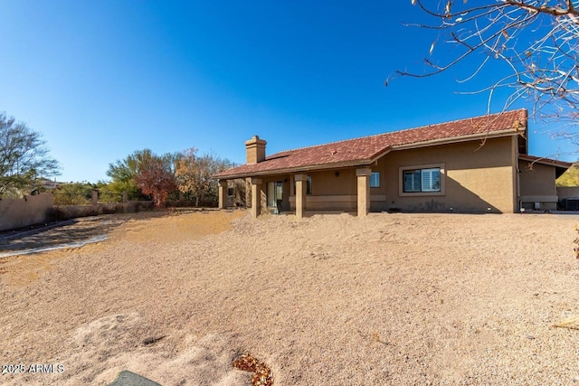 back of house featuring a chimney, fence, and stucco siding