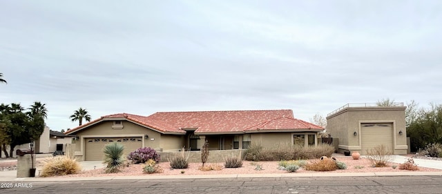 view of front of house featuring a garage, driveway, a tile roof, and stucco siding