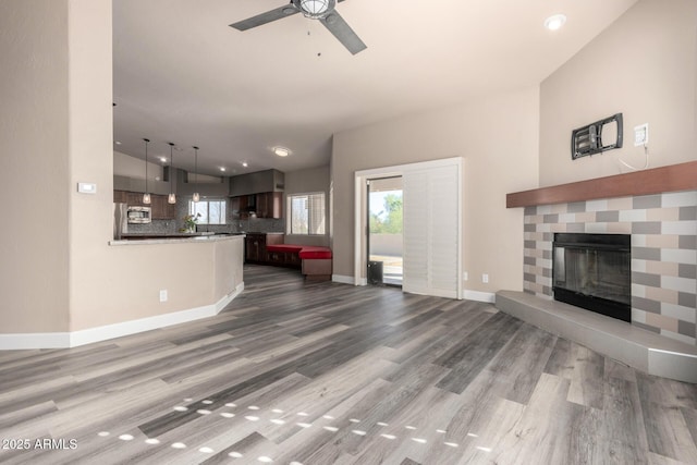 unfurnished living room featuring a ceiling fan, a fireplace, baseboards, and wood finished floors