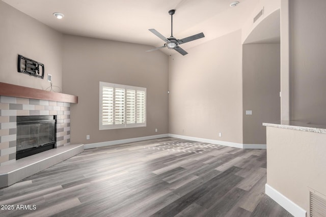 unfurnished living room with a fireplace, wood finished floors, a ceiling fan, and baseboards